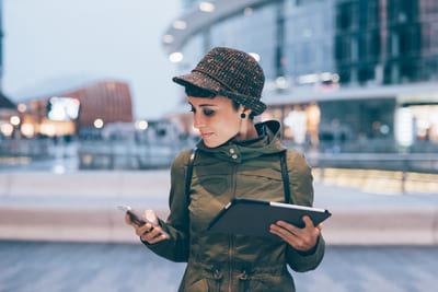 Frau mir Handy und Tablet in der Hand in der Stadt.